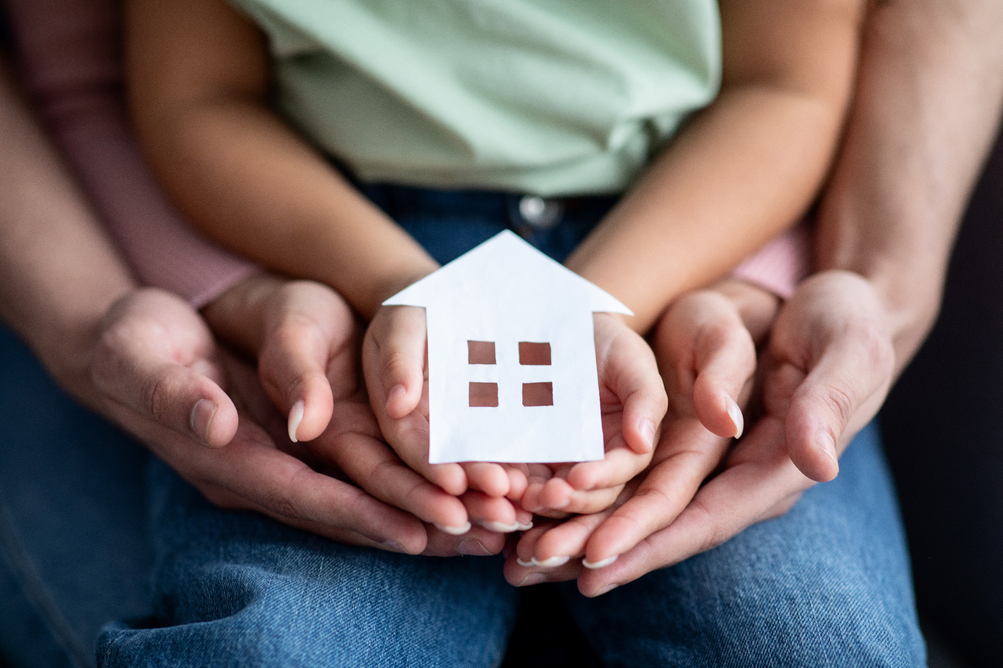 Mains grand-parents, parents et enfant tenant une maison symbolisant la donation pour l'achat d'un logement neuf